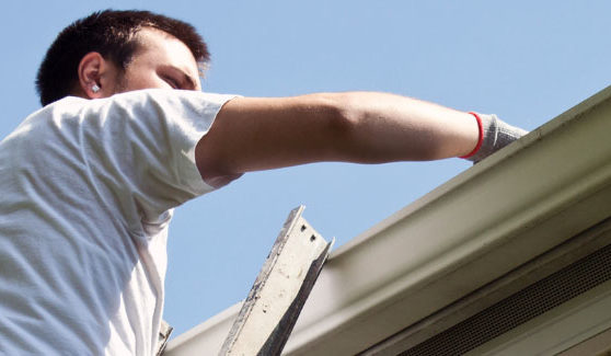 Man on a ladder cleaning out the gutters before hurricane season