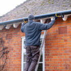 Man on a ladder fixing fitting a rain gutter