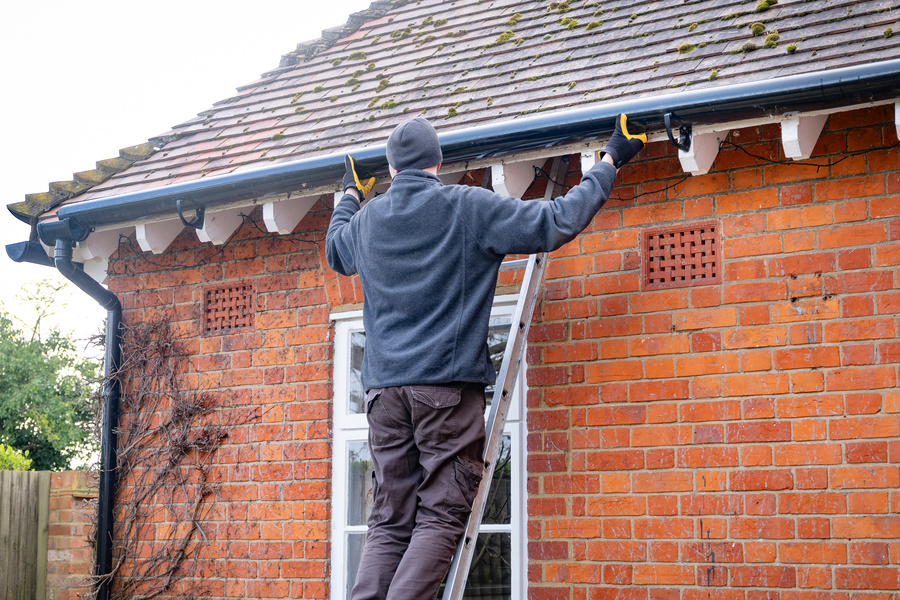 Man on a ladder fixing fitting a rain gutter