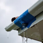 broken rain gutter, temporarily fixed with blue duct tape, is failing and leaking water, showing the need for proper home maintenance and repair