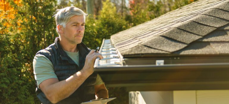 man standing on steps inspecting house roof gutter and leaf guard
