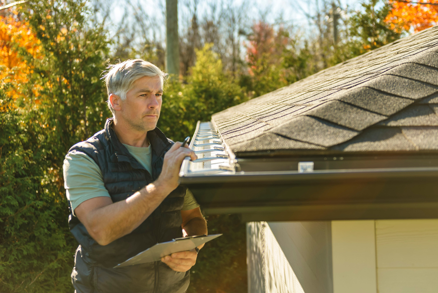 man standing on steps inspecting house roof gutter and leaf guard