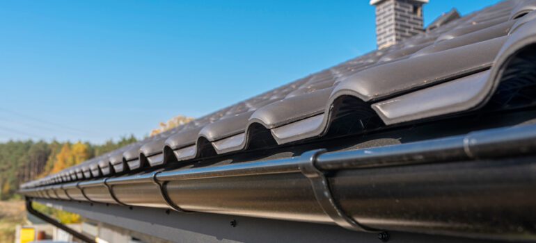 A metal, black gutter on a roof covered with ceramic tiles