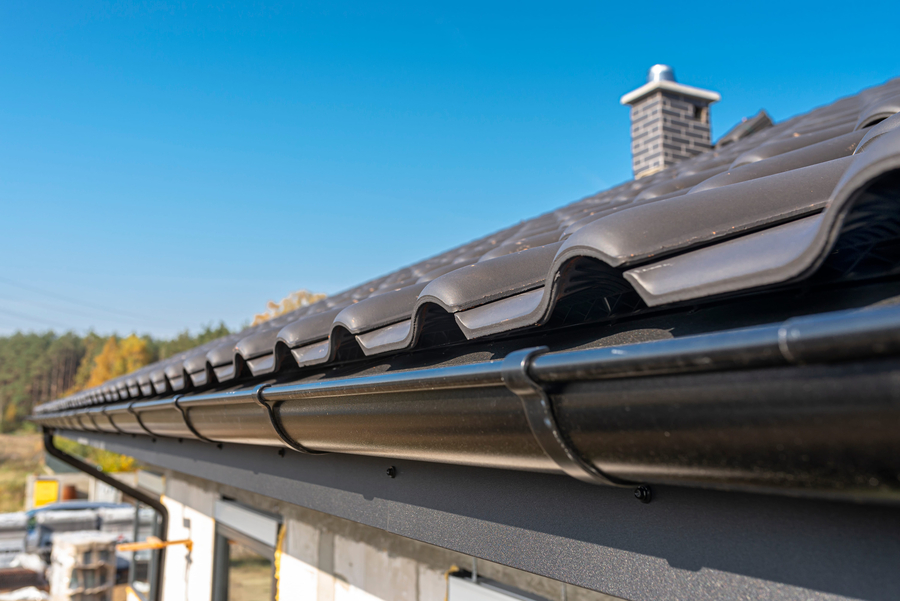 A metal, black gutter on a roof covered with ceramic tiles